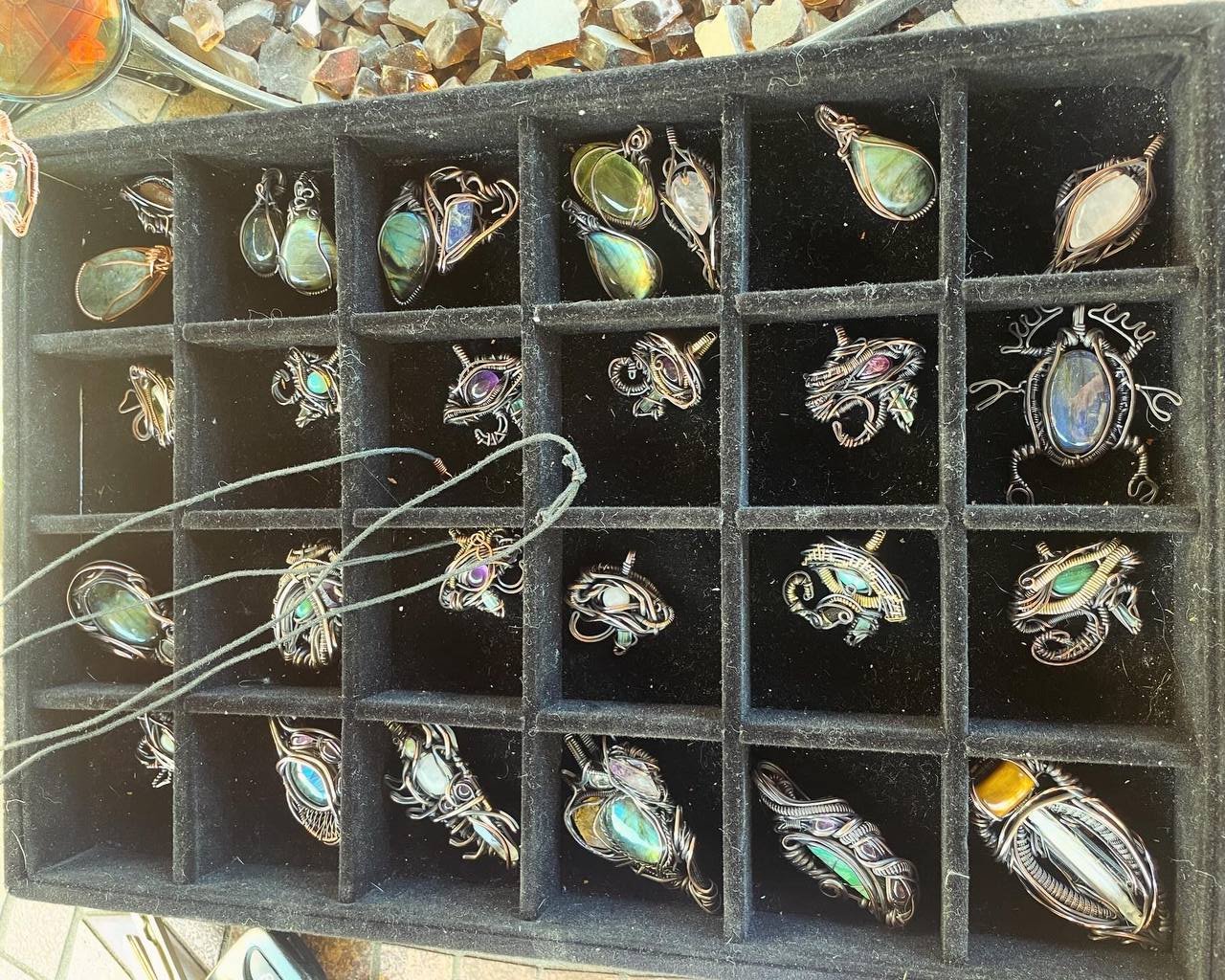 A display tray showcasing a collection of Jujusols' custom wire-wrapped jewelry, featuring intricate designs with gemstones and crystals in various shapes and sizes